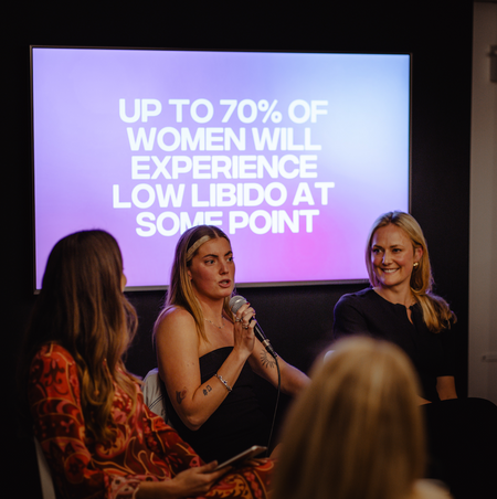 A shot from the HANX x Service95 Libido Event, featuring sex educator EmmCheeky speaking into a microphone, against a purple screen which reads 'Up to 70% of Women will experience low libido at some point'